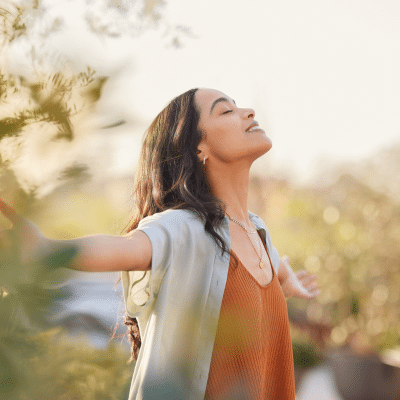 Woman outside in nature with arms out and head up, soaking it all in, representing mindfulness meditation